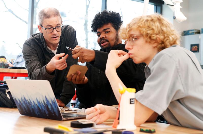 Students in a classroom with their professor working over a laptop